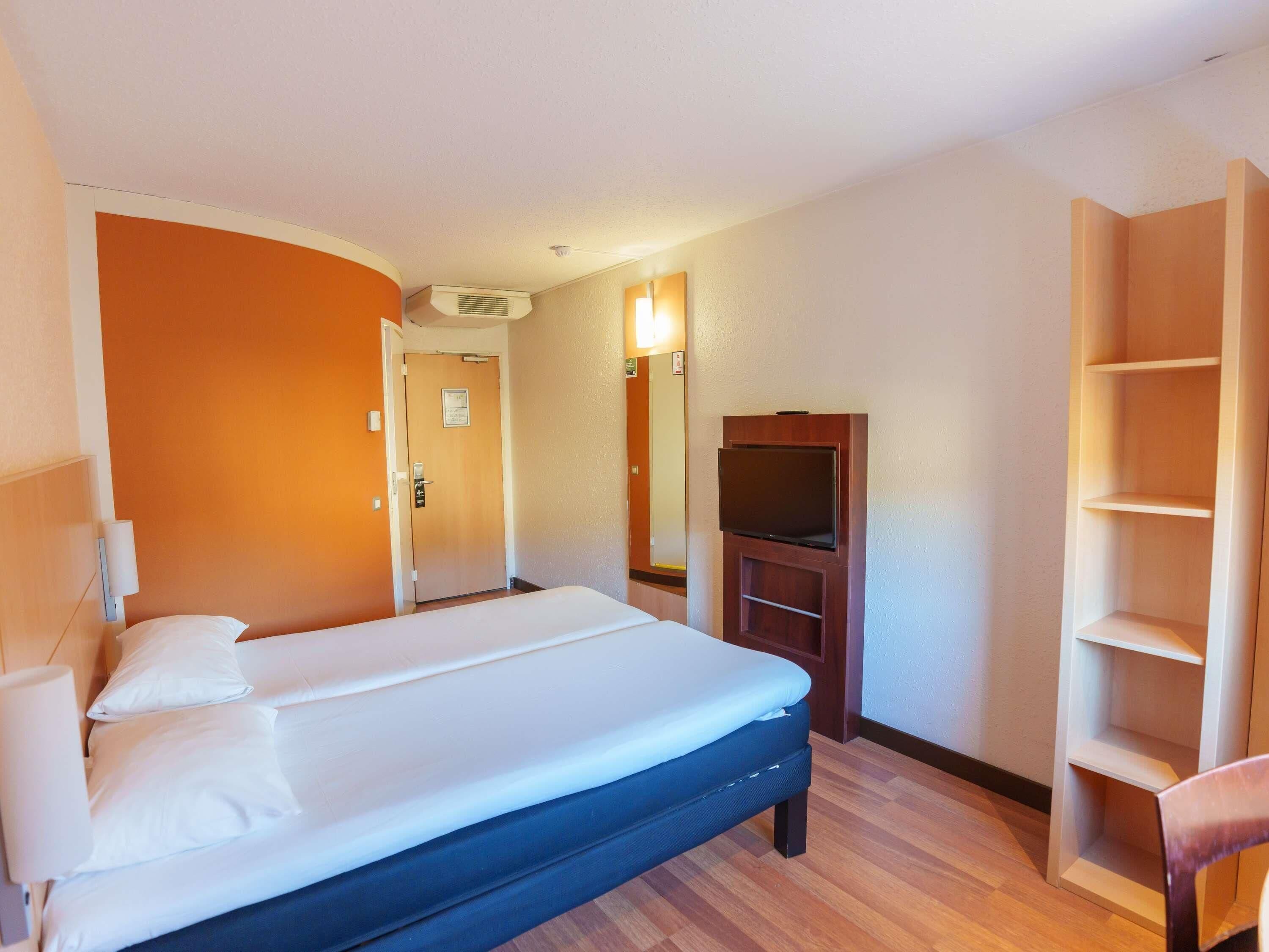 Una habitación de hotel con una cama, un televisor, un armario y una puerta que da a otra habitación.