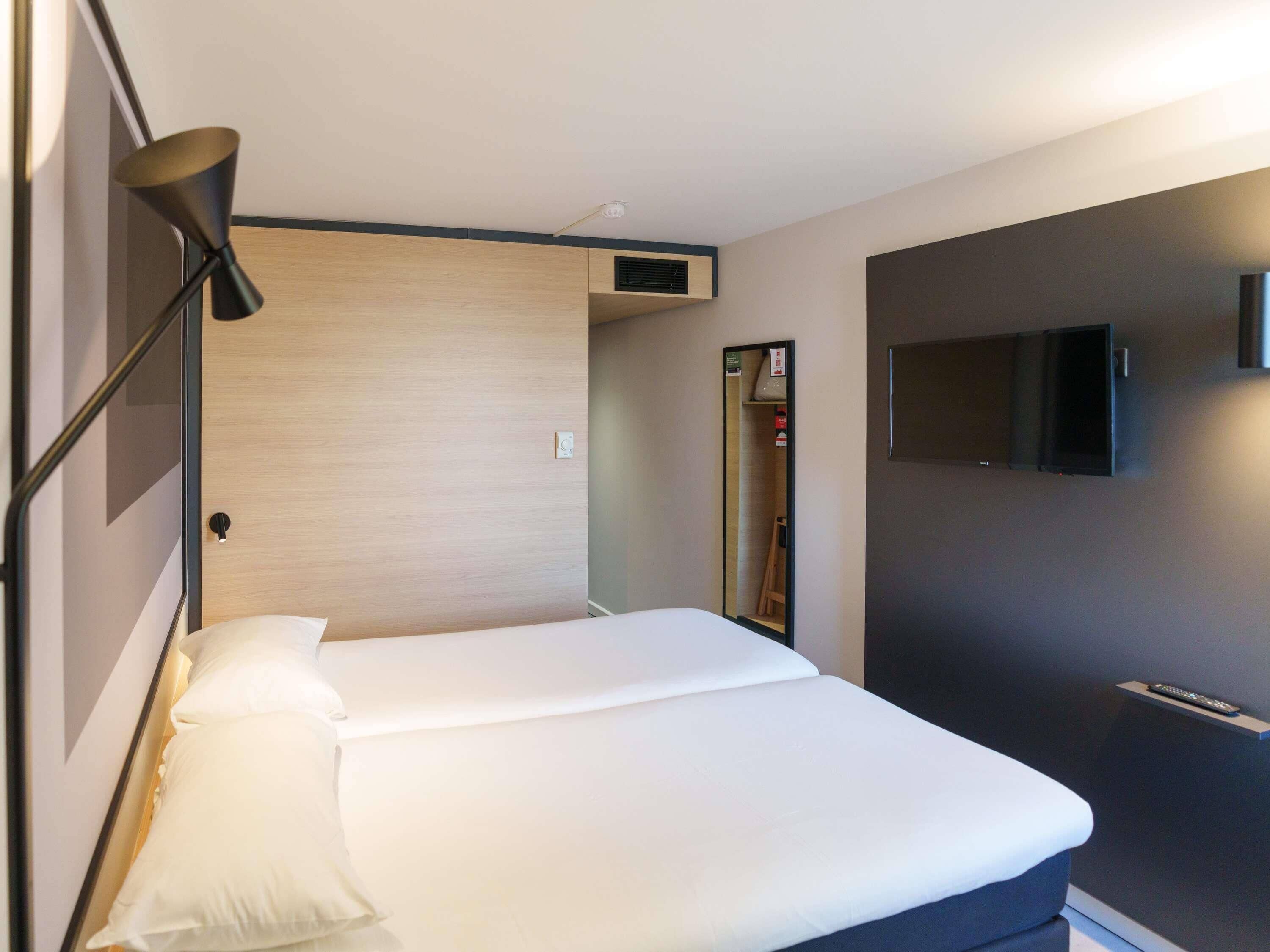 Una habitación de hotel con una cama, un televisor instalado en la pared y una puerta que da a un baño.