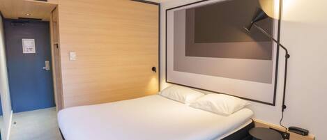 A modern bedroom with a bed, a bedside table with a lamp, and a door leading to another room.