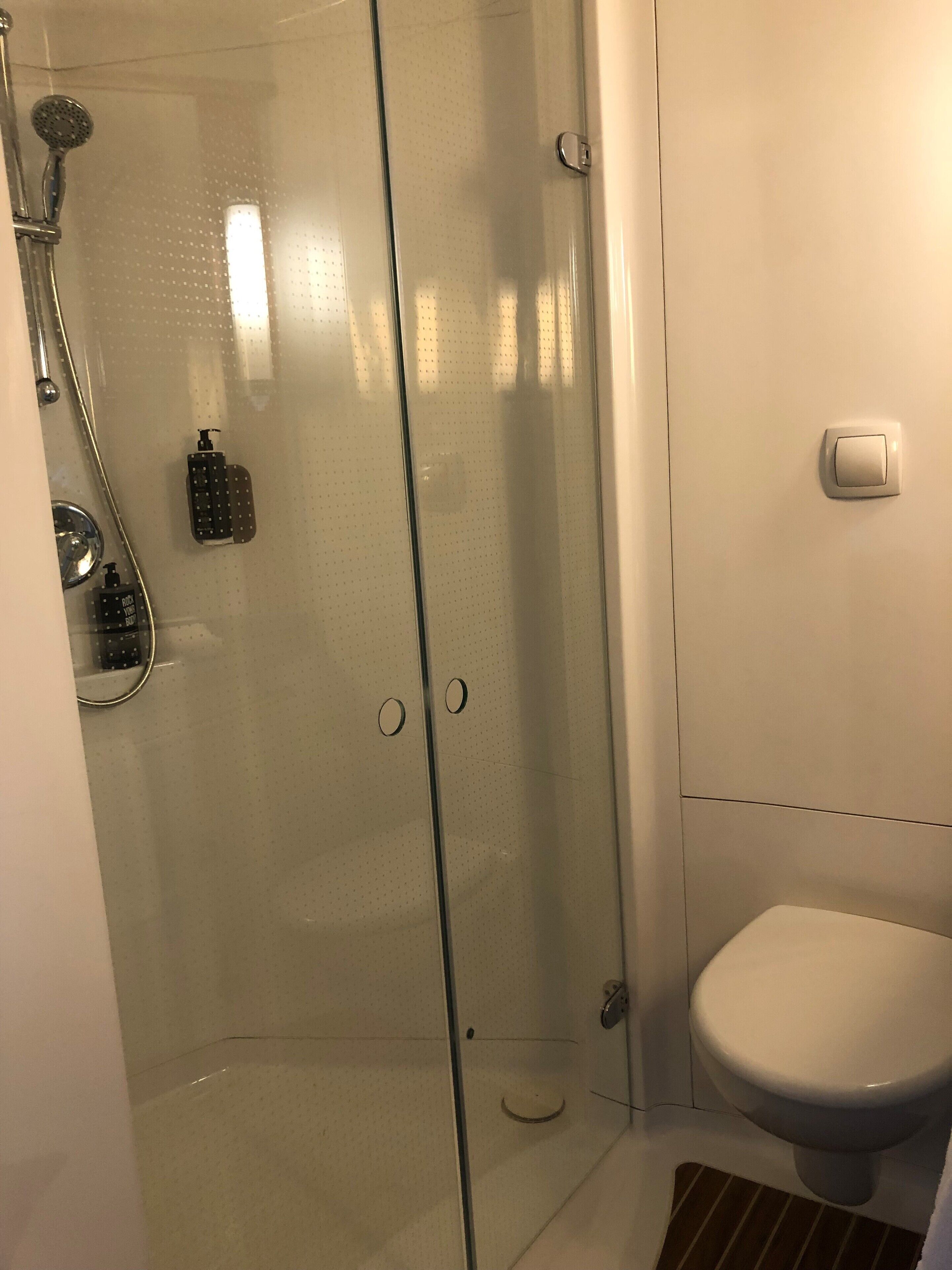 A bathroom with a glass shower enclosure, a toilet, and a sink with soap dispensers.