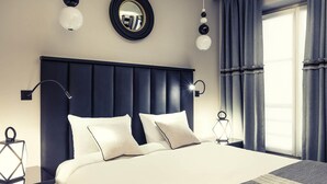 Una habitación de hotel moderna con una cama grande, cabecero oscuro y un ventanal con cortinas.