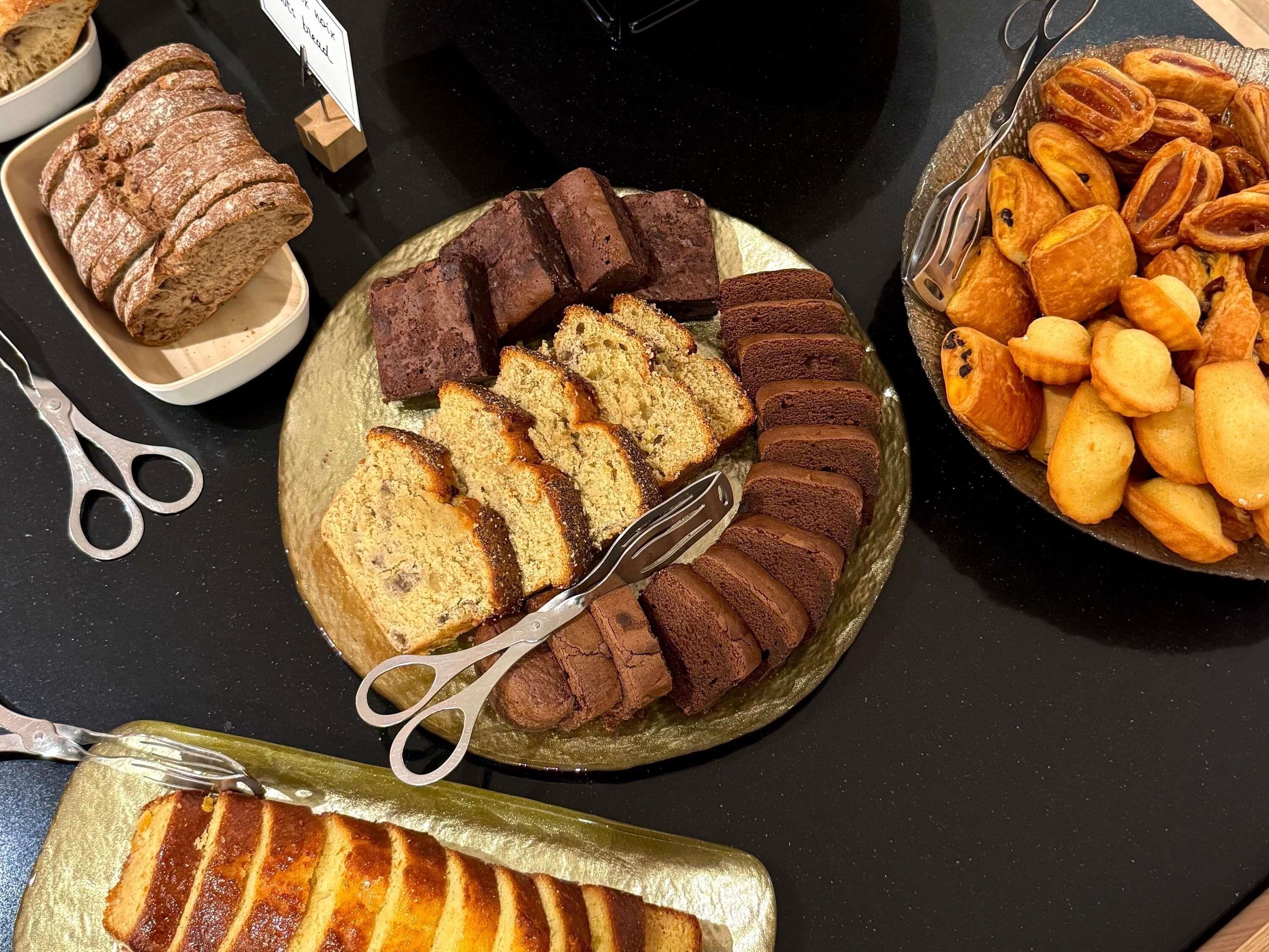 A variety of baked goods on a table, including sliced bread, brownies, and pastries.
