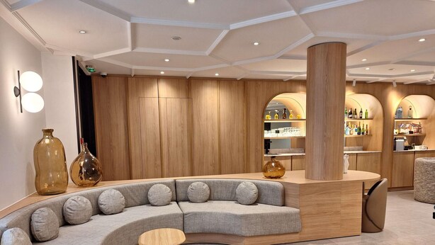 Un interior moderno con una zona de estar curva, paneles de madera y una barra con estantes llenos de botellas.