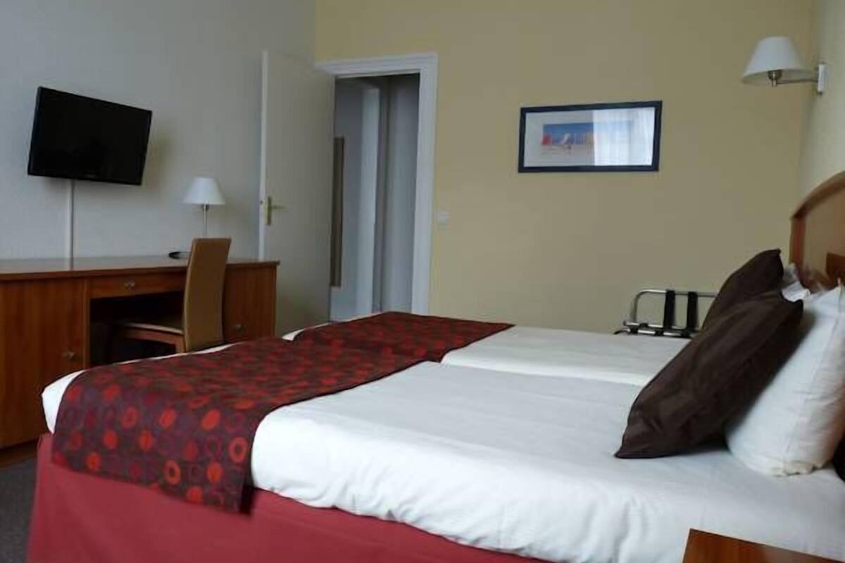 Une chambre d’hôtel avec un lit, un bureau, une chaise, une télévision et une porte.