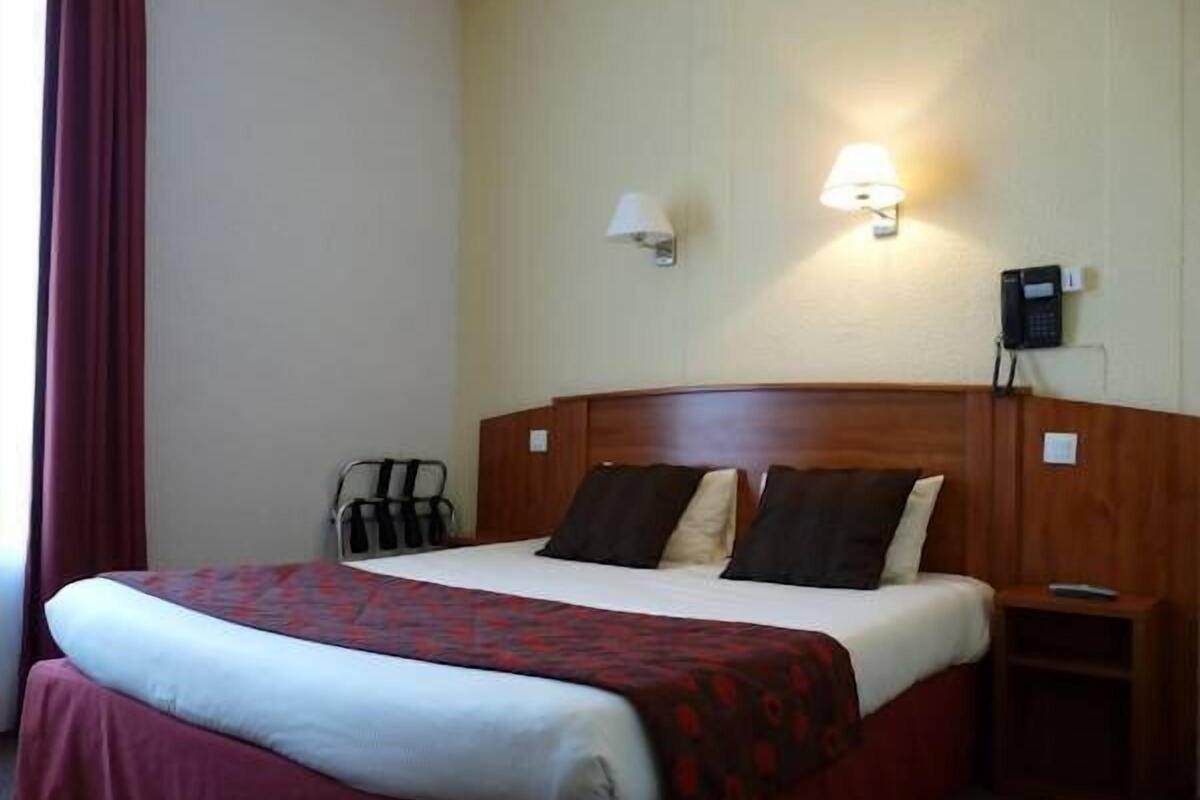Une chambre d’hôtel avec un lit, une table de chevet, une lampe et un téléphone.