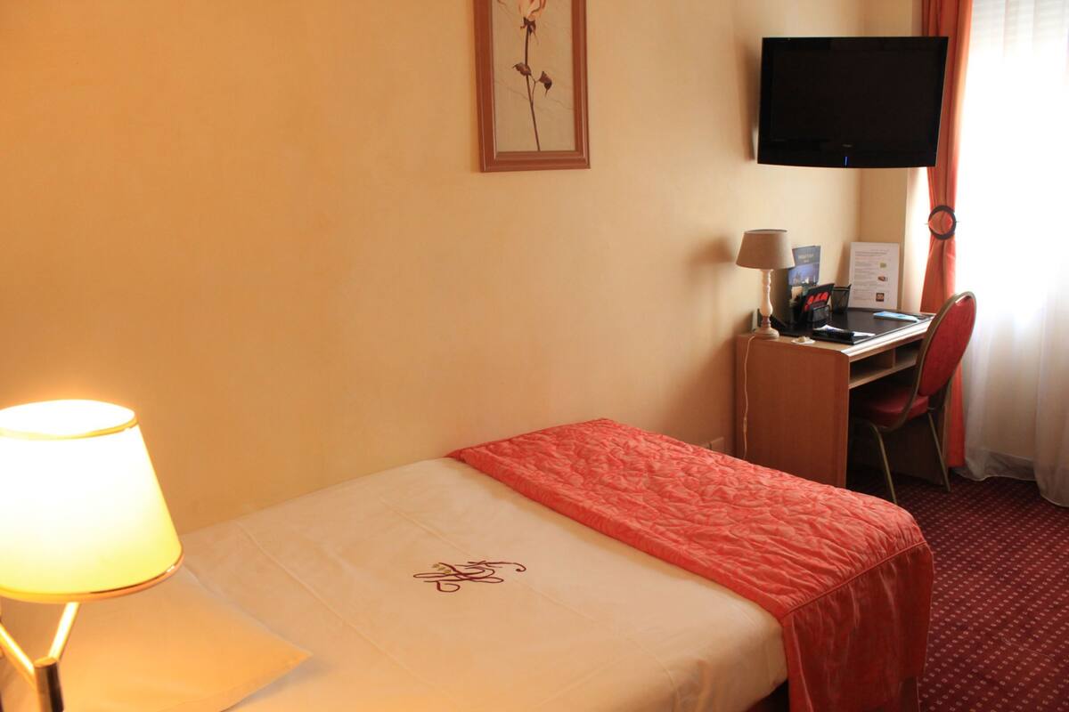 A hotel room with a bed, a desk, a chair, a television, and a lamp.