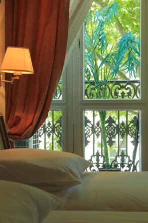 A bedroom with a bed, a lamp, and a window with a view of greenery. - Hotel Foch (Lyon)