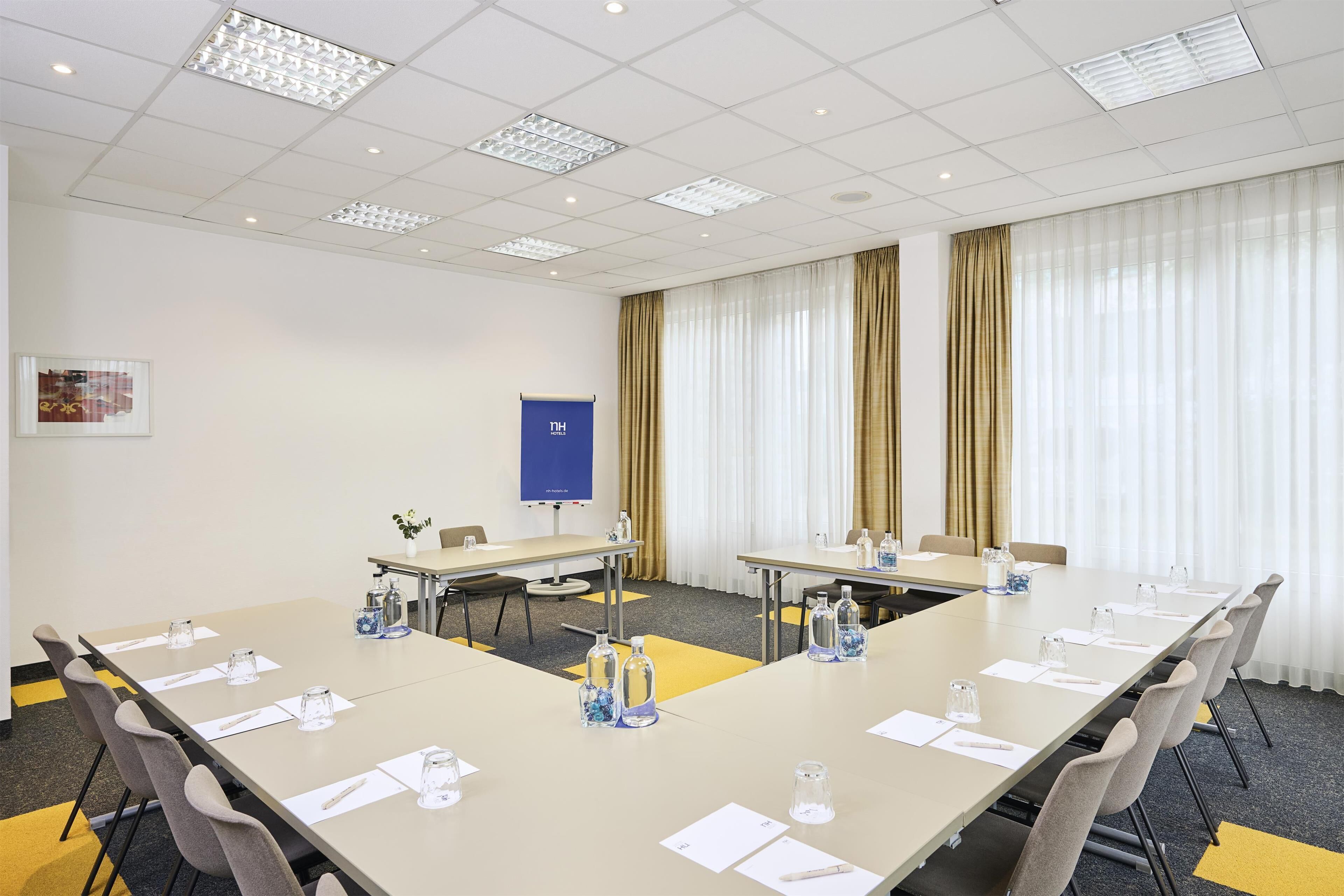 A conference room with a long table, chairs, water bottles, and a blue sign on the wall.