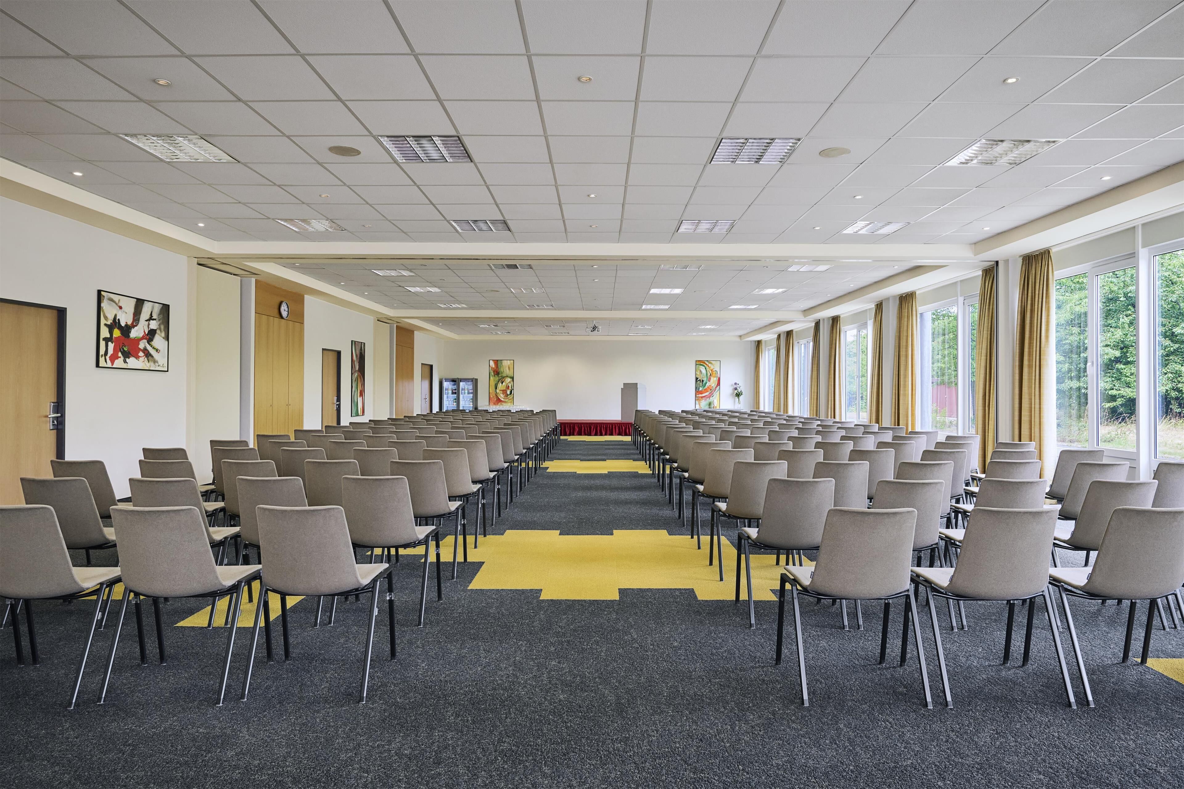 Ein Konferenzraum mit Reihen von Stühlen, einem gelben Teppich und großen Fenstern.