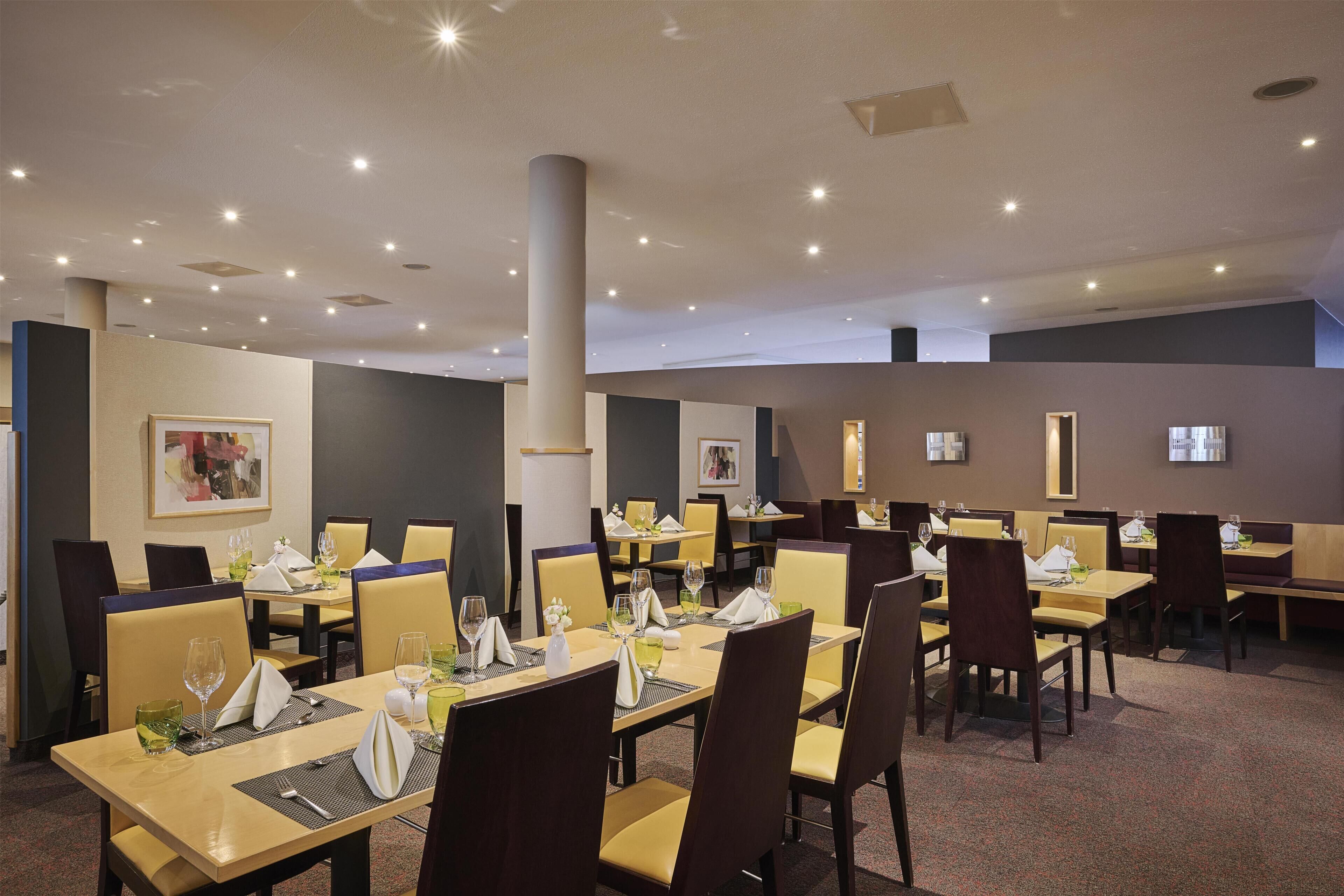 A hotel dining area with multiple tables and chairs, arranged in a spacious layout.