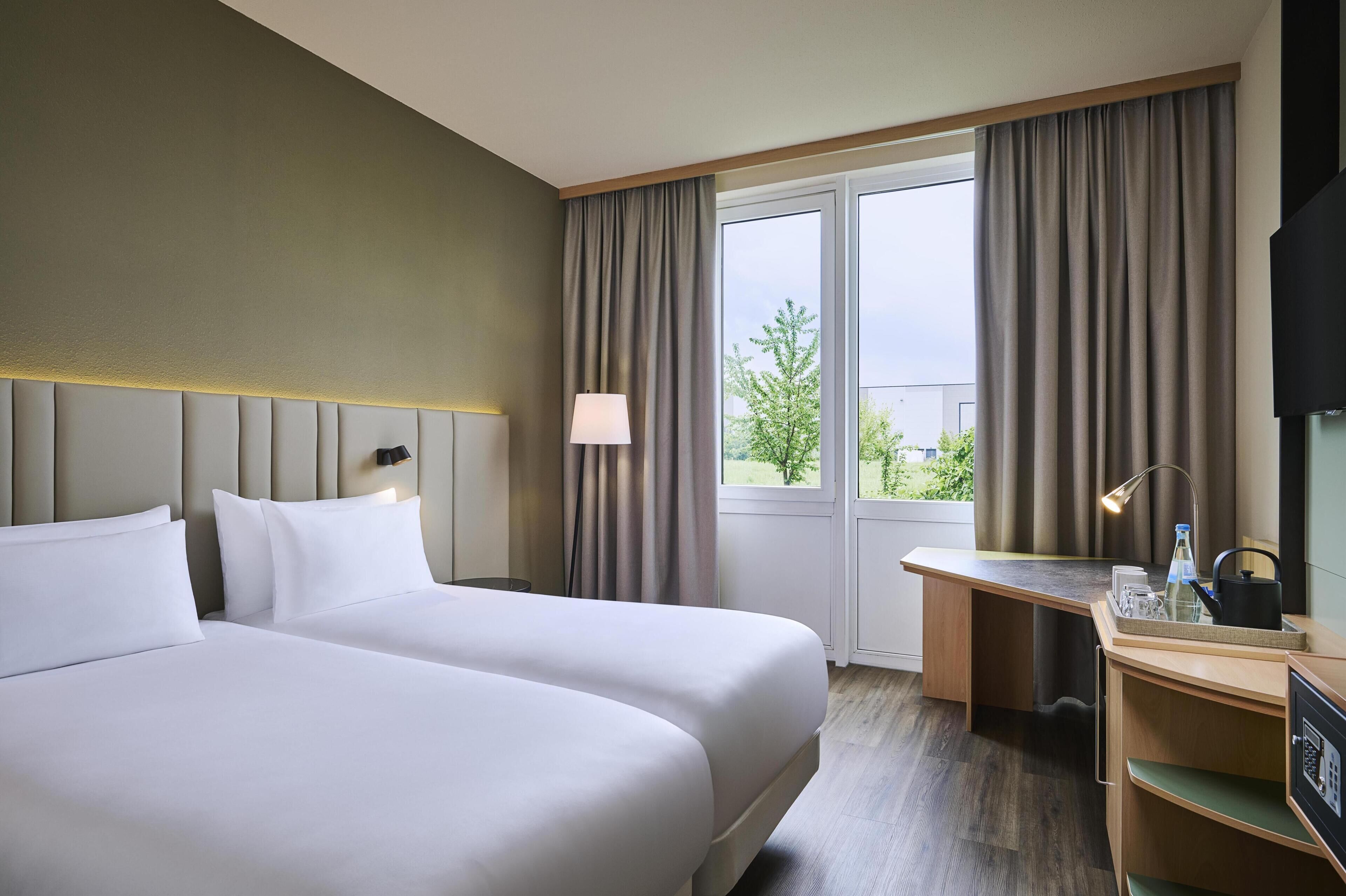 Habitación de hotel con dos camas, un escritorio, una silla, un televisor y una ventana con cortinas.