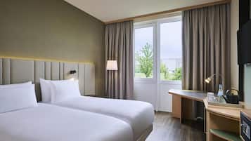 Ein Hotelzimmer mit zwei Betten, einem Schreibtisch, einem Stuhl, einem Fernseher und einem Fenster mit Vorhängen.