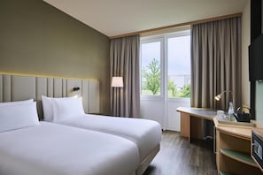 Ein Hotelzimmer mit zwei Betten, einem Schreibtisch, einem Stuhl, einem Fernseher und einem Fenster mit Vorhängen.