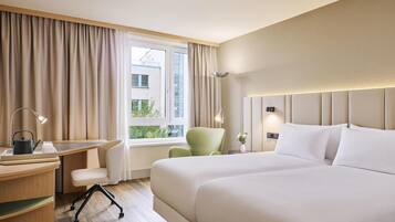 A hotel room with a bed, desk, chair, lamp, and window with curtains.