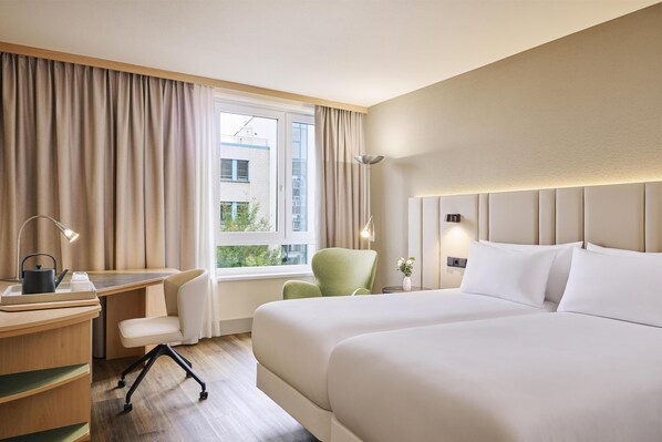 A hotel room with a bed, desk, chair, lamp, and window with curtains.