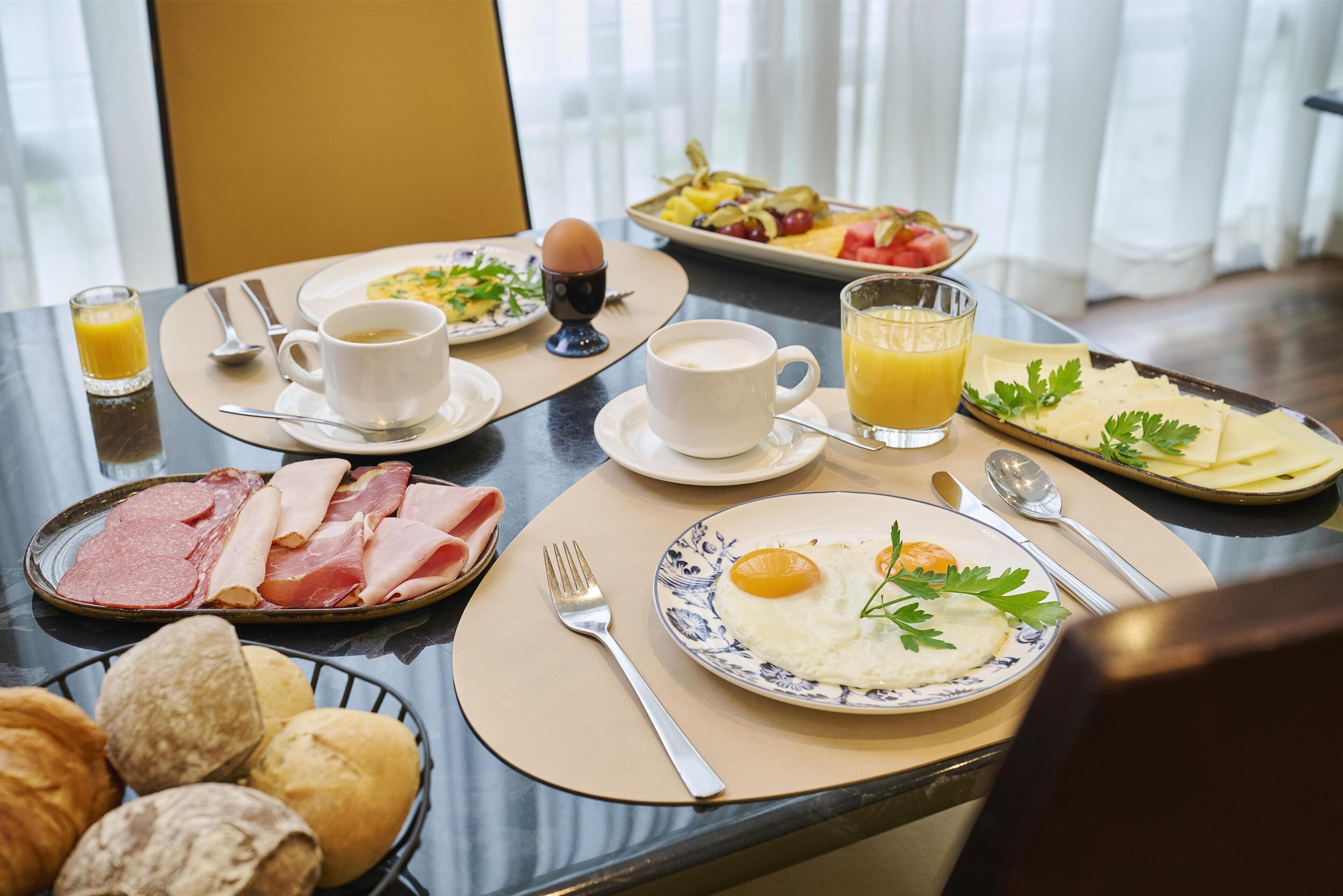 Una mesa de desayuno con diversos alimentos, como huevos, jamón, pan y jugo.