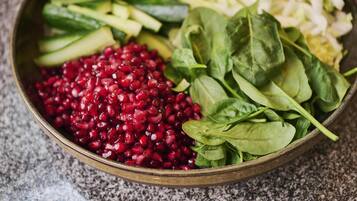 A bowl containing sliced cucumbers, shredded cabbage, spinach leaves, and pomegranate seeds.