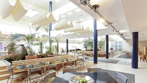 A spacious indoor area with multiple seating arrangements, including tables and benches, surrounded by potted plants. - Hotel Watthalden (Ettlingen)