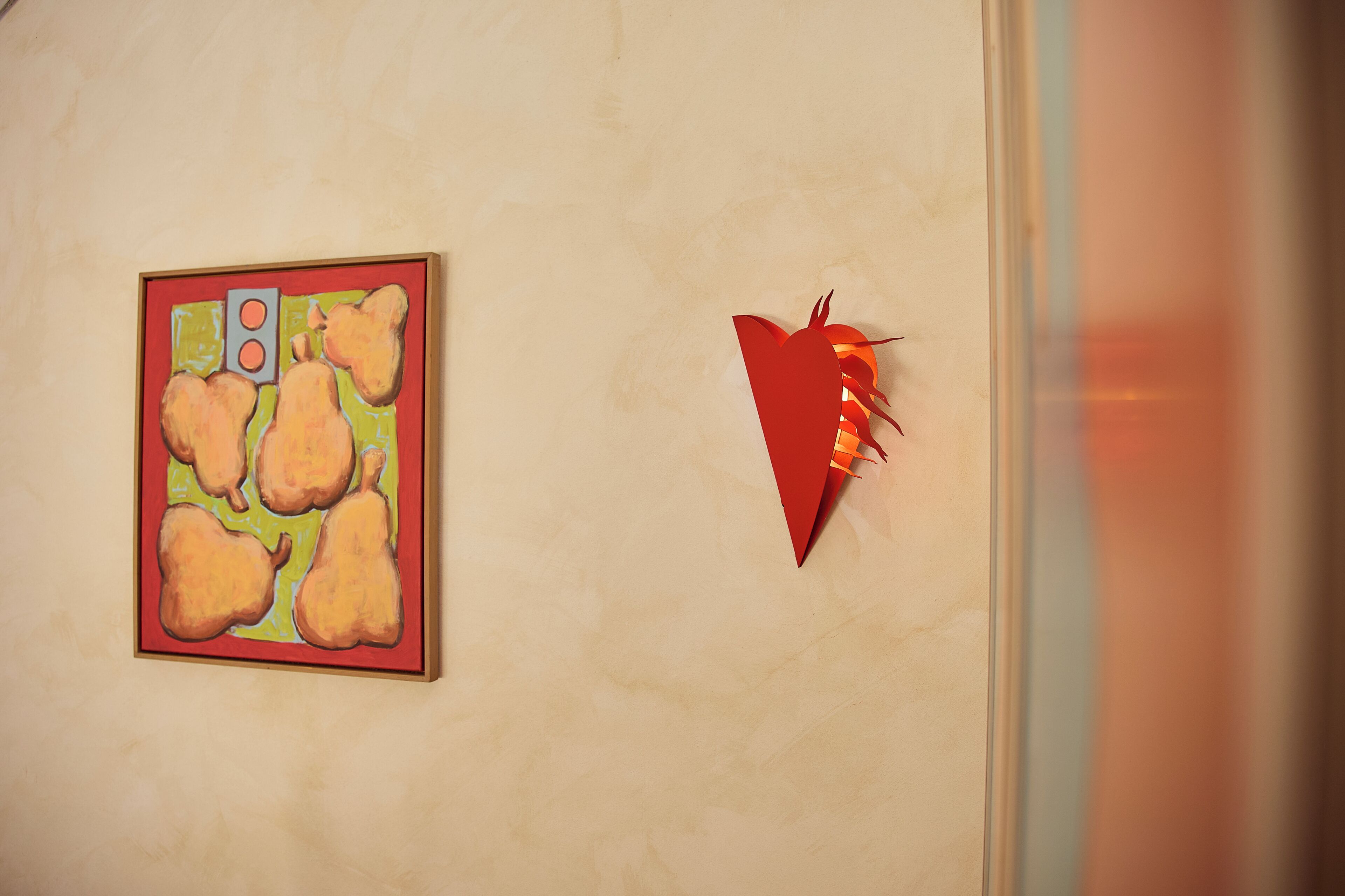A wall with a framed artwork of pears and a red paper airplane.