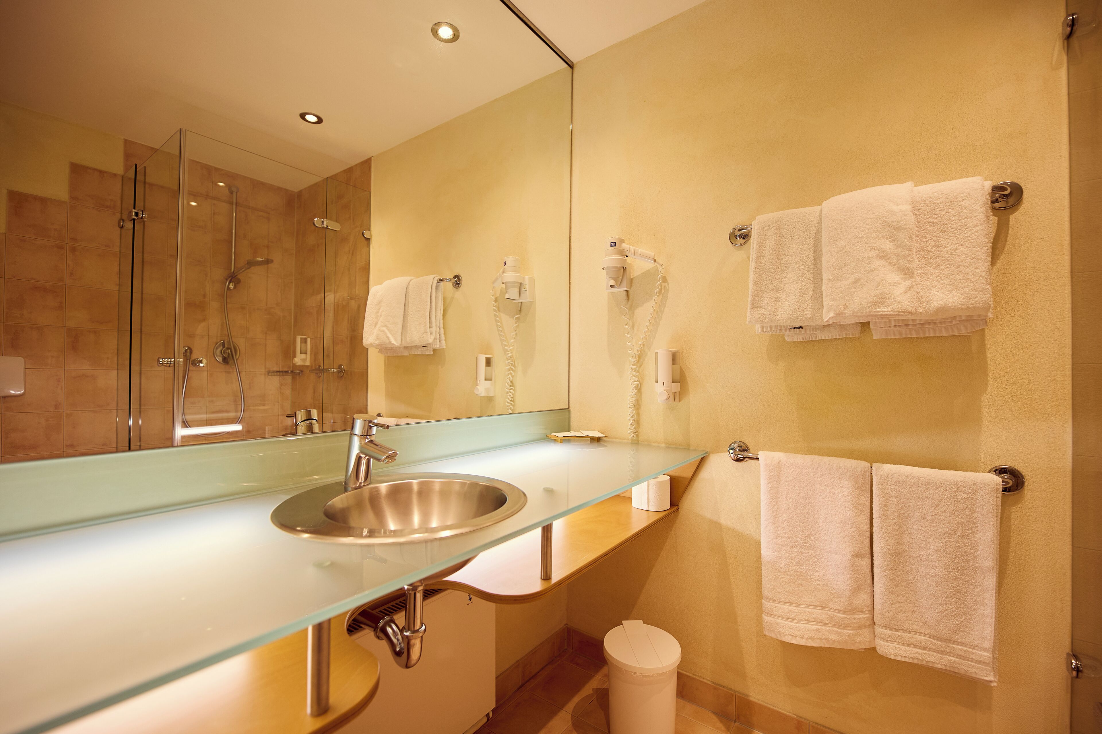 Ein modernes Badezimmer mit einem Waschbecken aus Glas, einer Dusche und zwei Handtüchern, die an der Wand hängen.