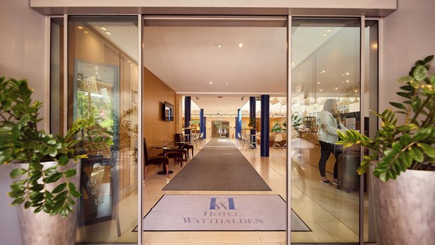 A hotel entrance with a clear view of the interior, including a reception desk, seating area, and a visible plant. - Hotel Watthalden (Ettlingen)