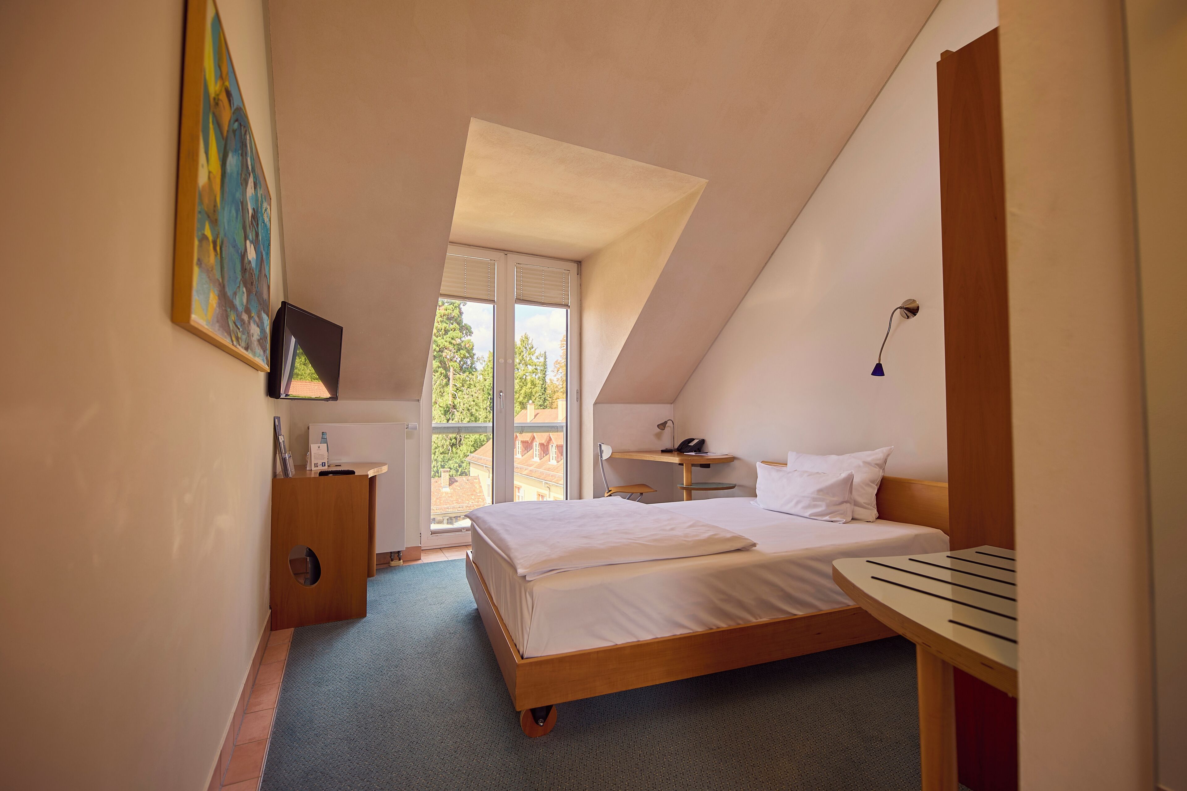 A bedroom with a bed, a desk, a chair, a window, and a painting on the wall.