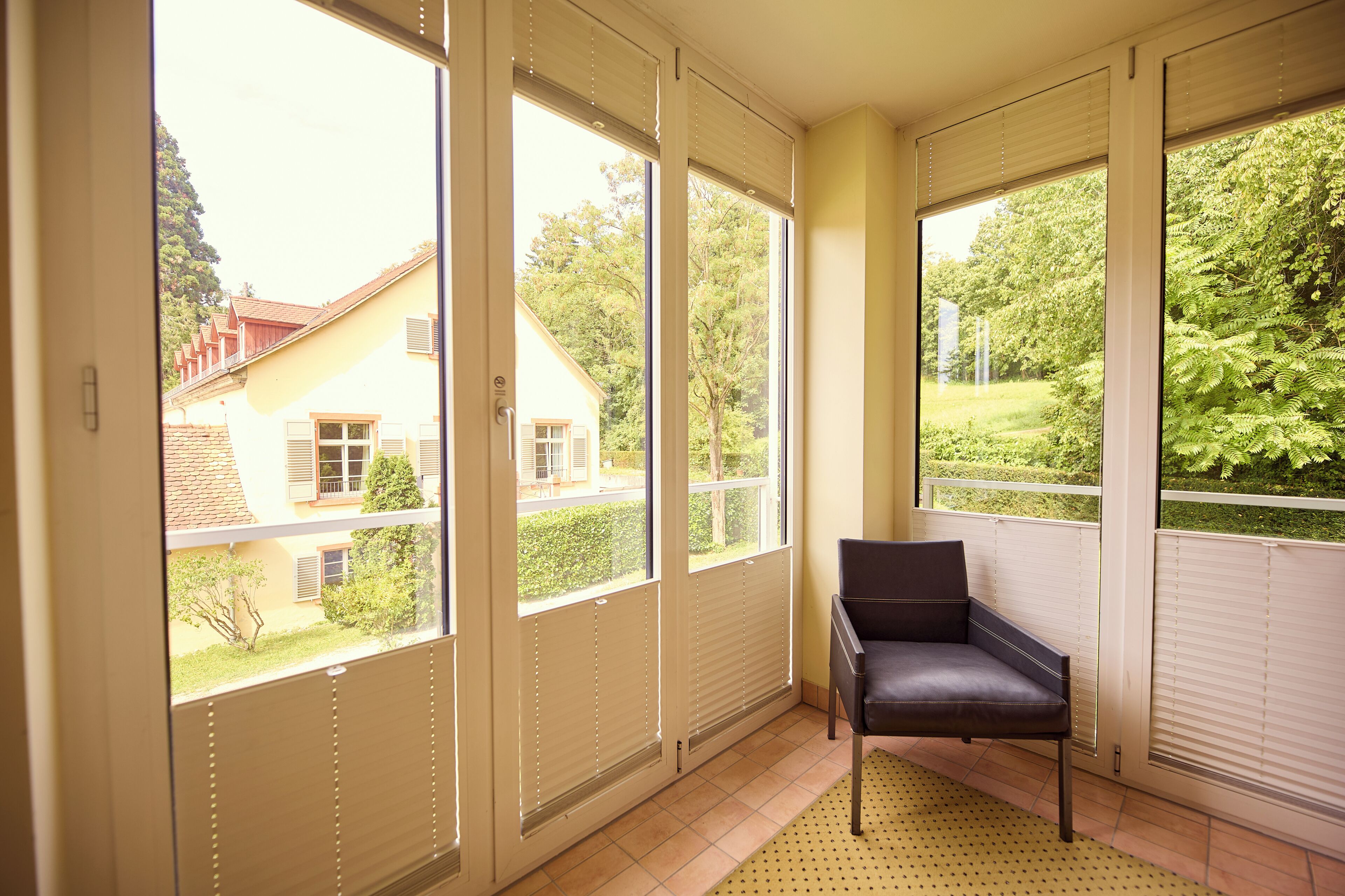 A room with large windows, a chair, and a tiled floor.