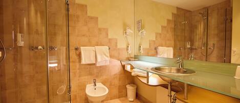 A modern bathroom with a glass shower enclosure, a pedestal sink, a bidet, and a large mirror.