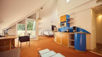 A spacious room with a bed, a desk, a chair, a blue accent wall, and a large window.