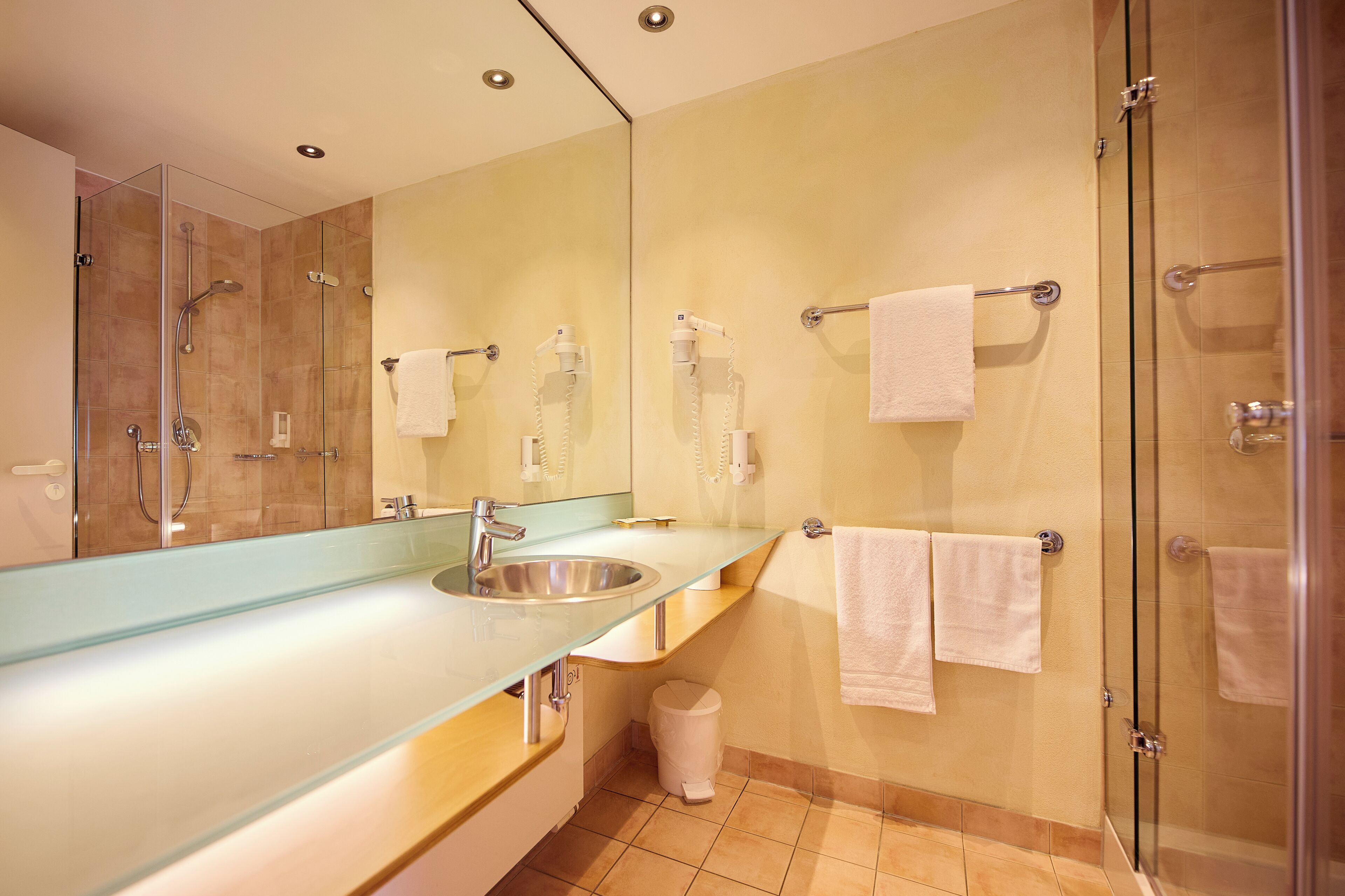 A modern bathroom with a glass shower enclosure, a sink with a glass countertop, and a large mirror.