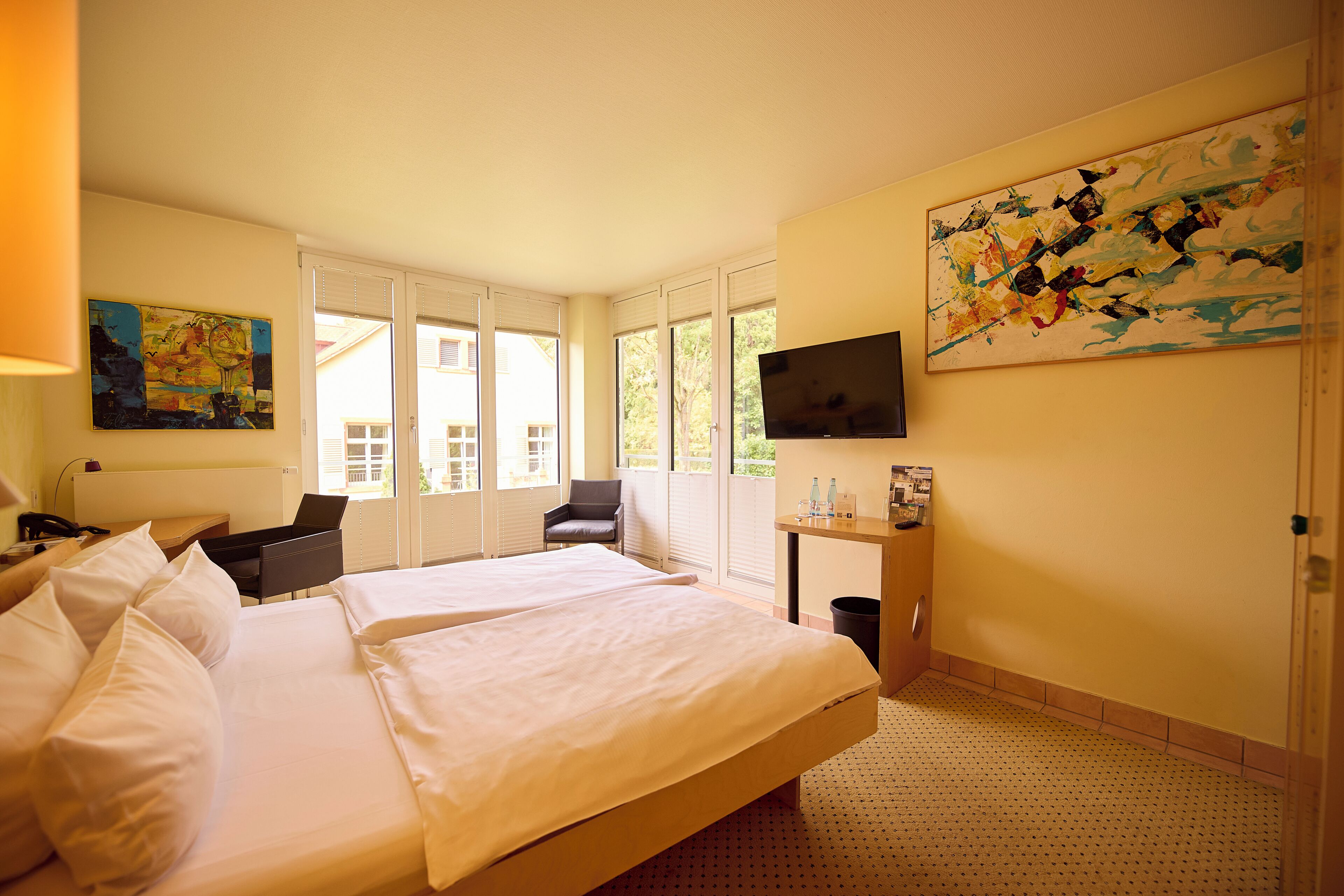 Ein Hotelzimmer mit einem großen Bett, einem Schreibtisch, einem Stuhl, einem Fernseher und einem Fenster mit Jalousien.