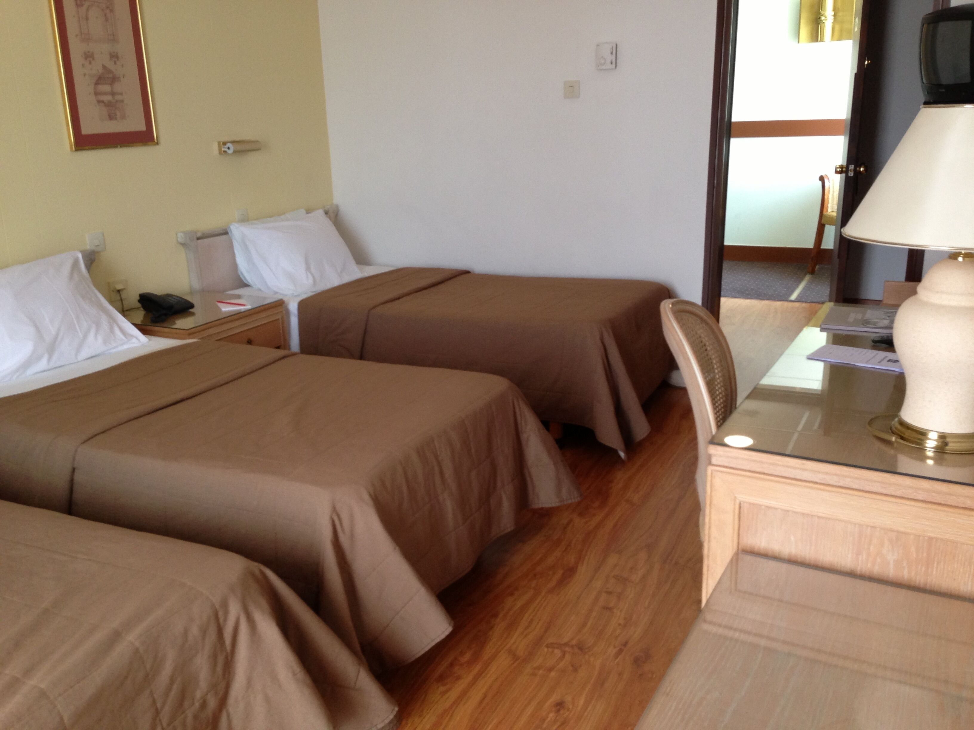 A hotel room with two single beds, a desk with a lamp, and a television.