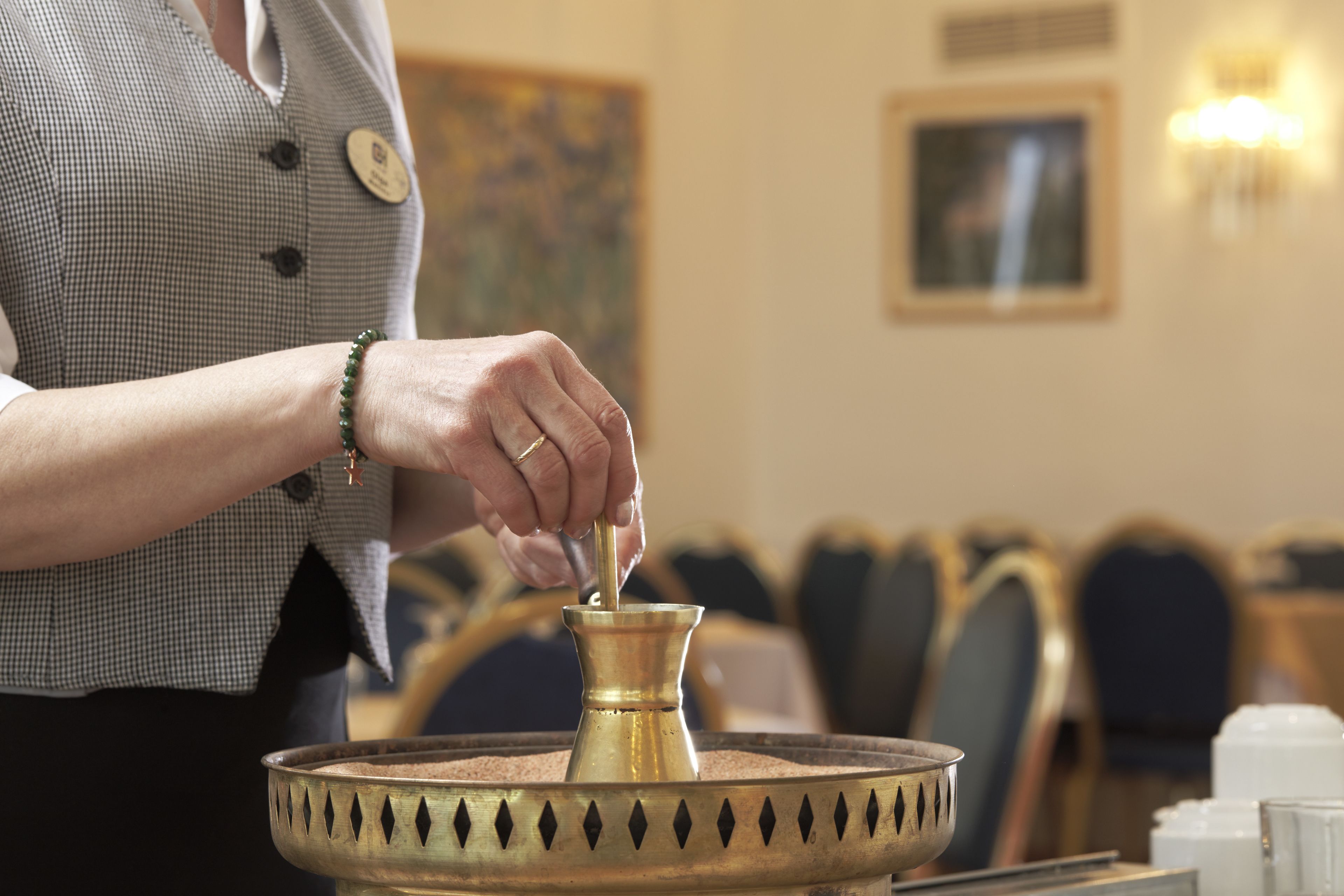 A person pouring a liquid from a brass container into a bowl.