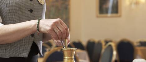 A person pouring a liquid from a brass container into a bowl.