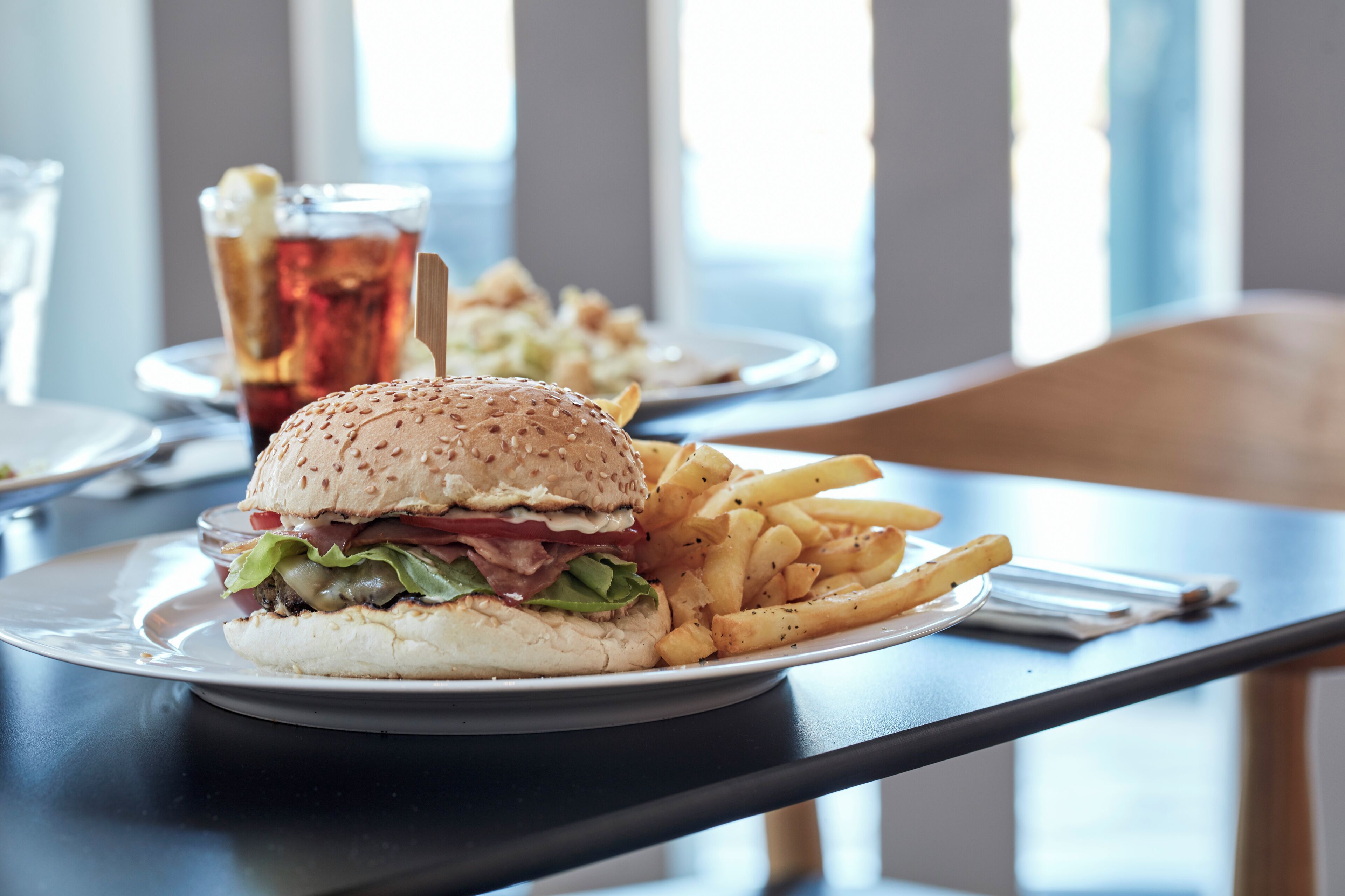 A dining table with a plate of food, including a burger and fries, and a glass of iced tea.
