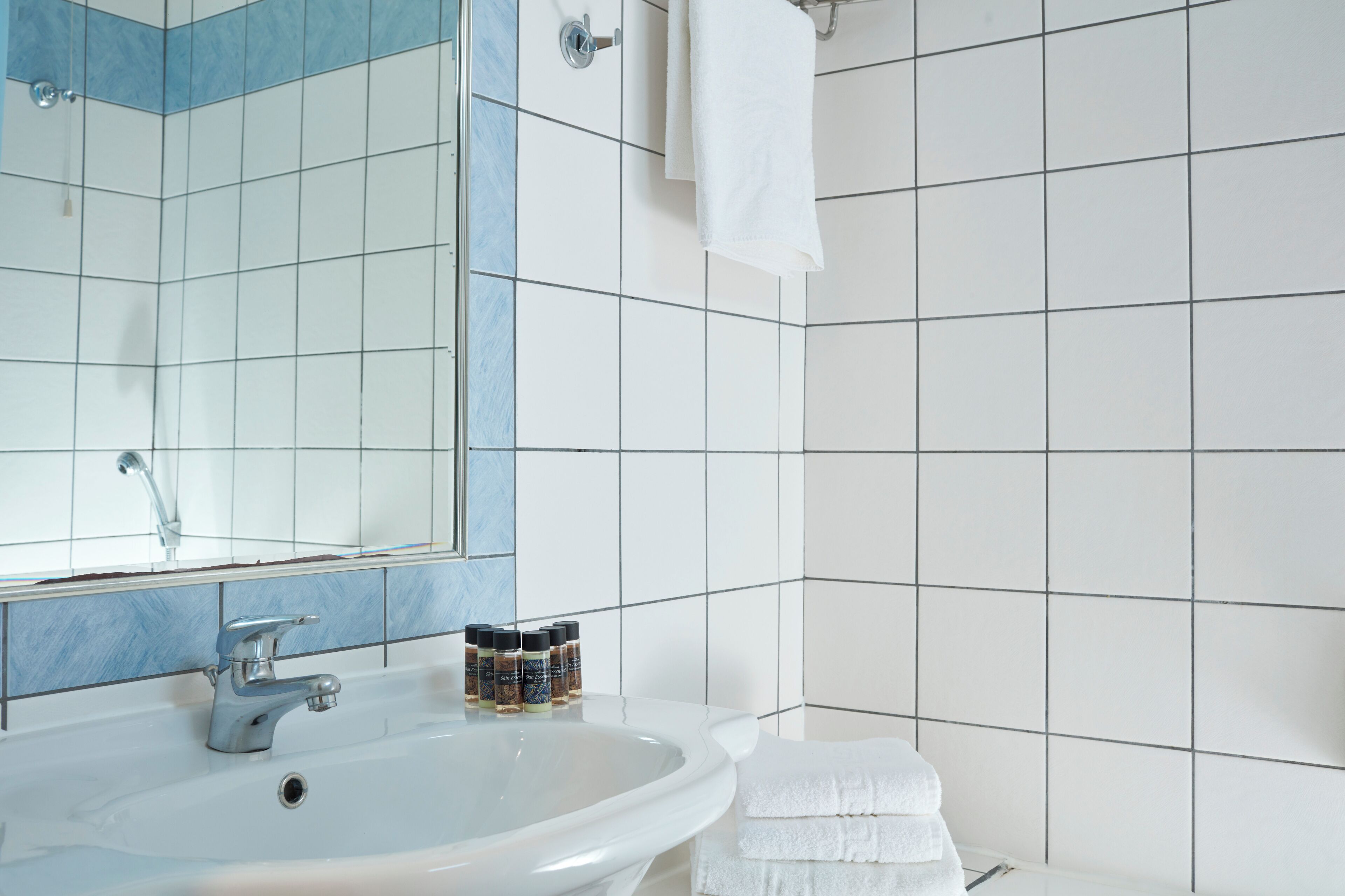 Een badkamer met een wit wastafelmeubel, een spiegel en een betegelde muur.