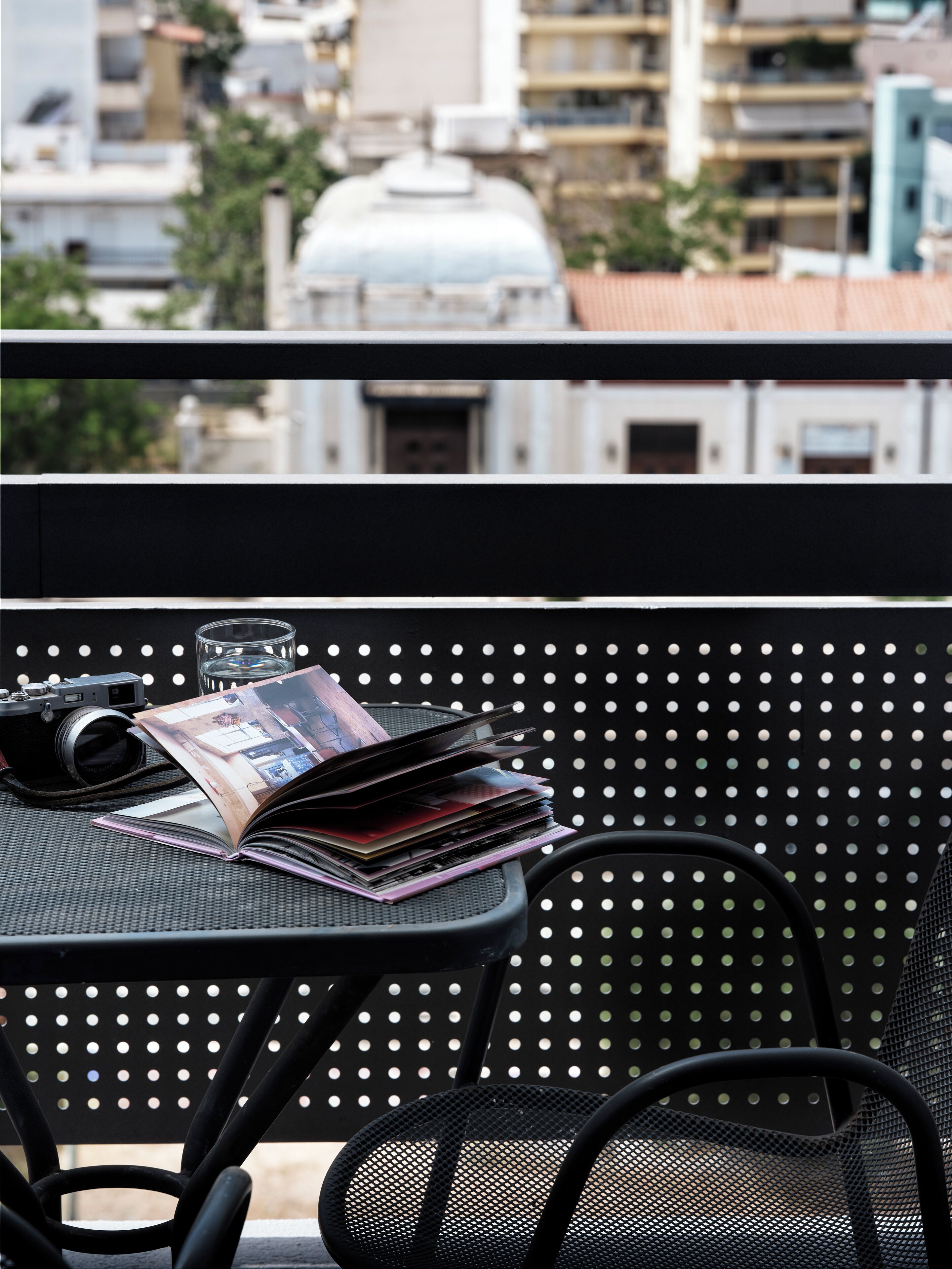Un balcón con una mesa que sostiene una cámara, un vaso y una revista.