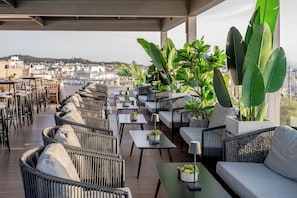Una terraza en la azotea con mobiliario de mimbre, plantas en macetas y vistas a la ciudad.