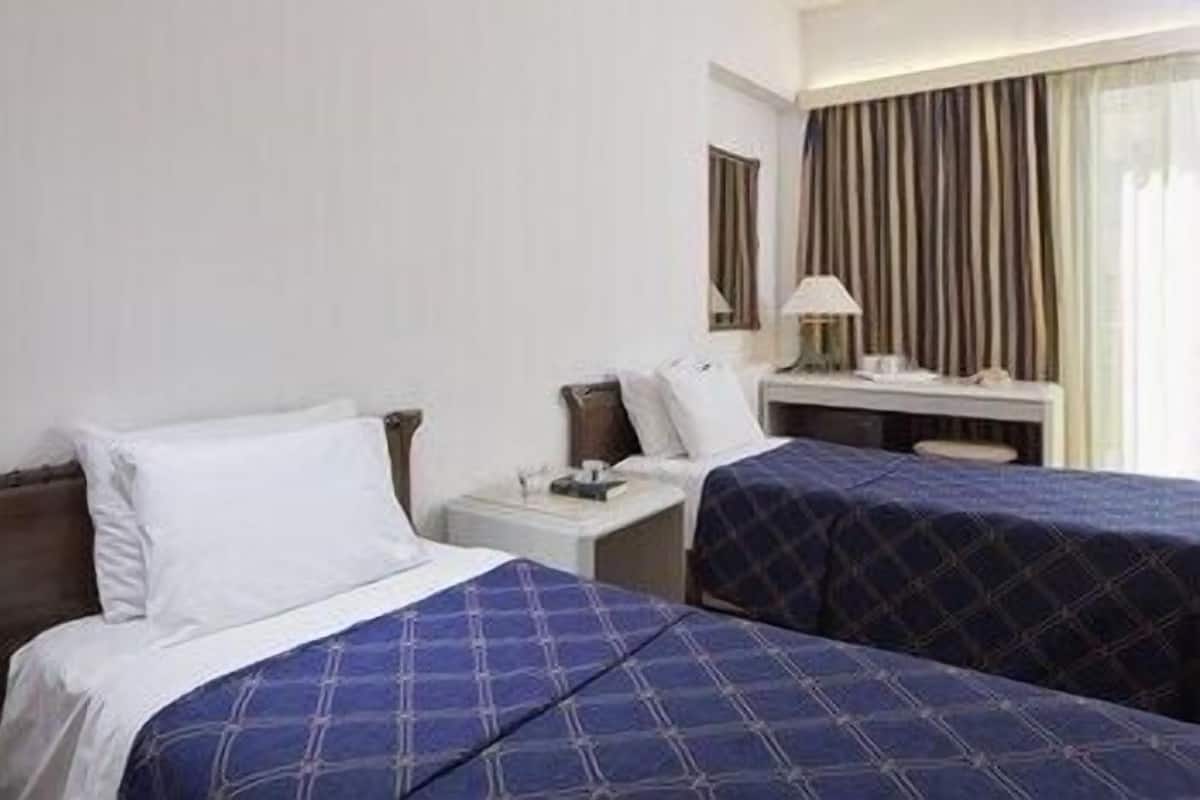 A hotel room with two beds, a desk, a lamp, and a window with curtains.