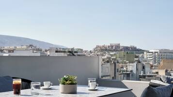 Terraza en la azotea con una mesa, dos tazas, un vaso de agua y una planta en maceta.