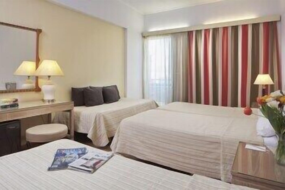 Una habitación de hotel con dos camas, un escritorio, una silla, una lámpara y una ventana con cortinas.