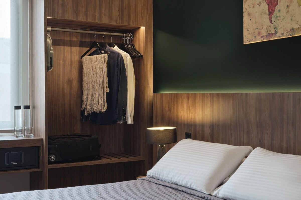 A hotel room with a bed, a wardrobe, a bedside table with a lamp, and a suitcase.