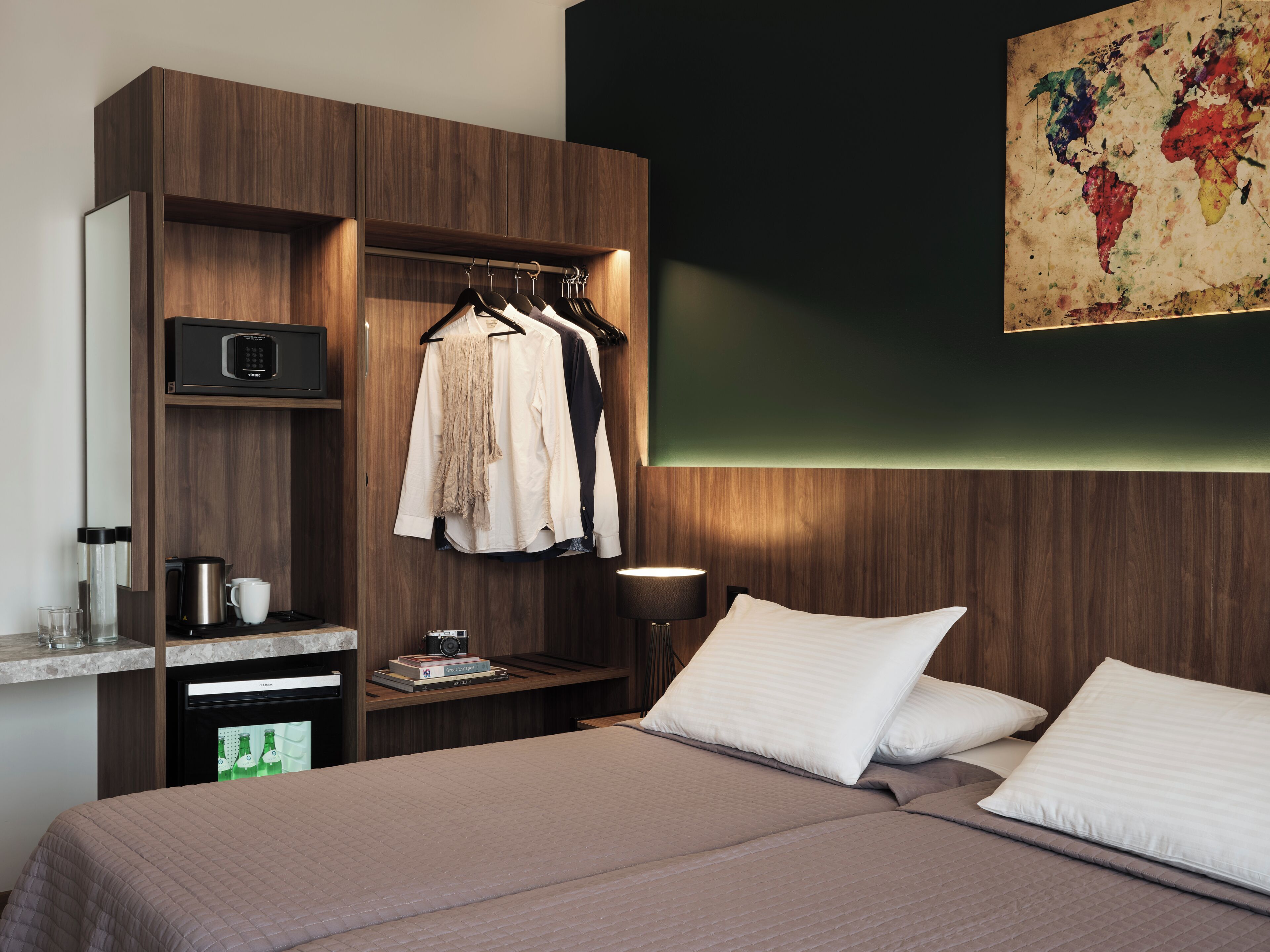 Une chambre d’hôtel avec un lit, une armoire, un bureau avec une machine à café et une carte accrochée au mur.