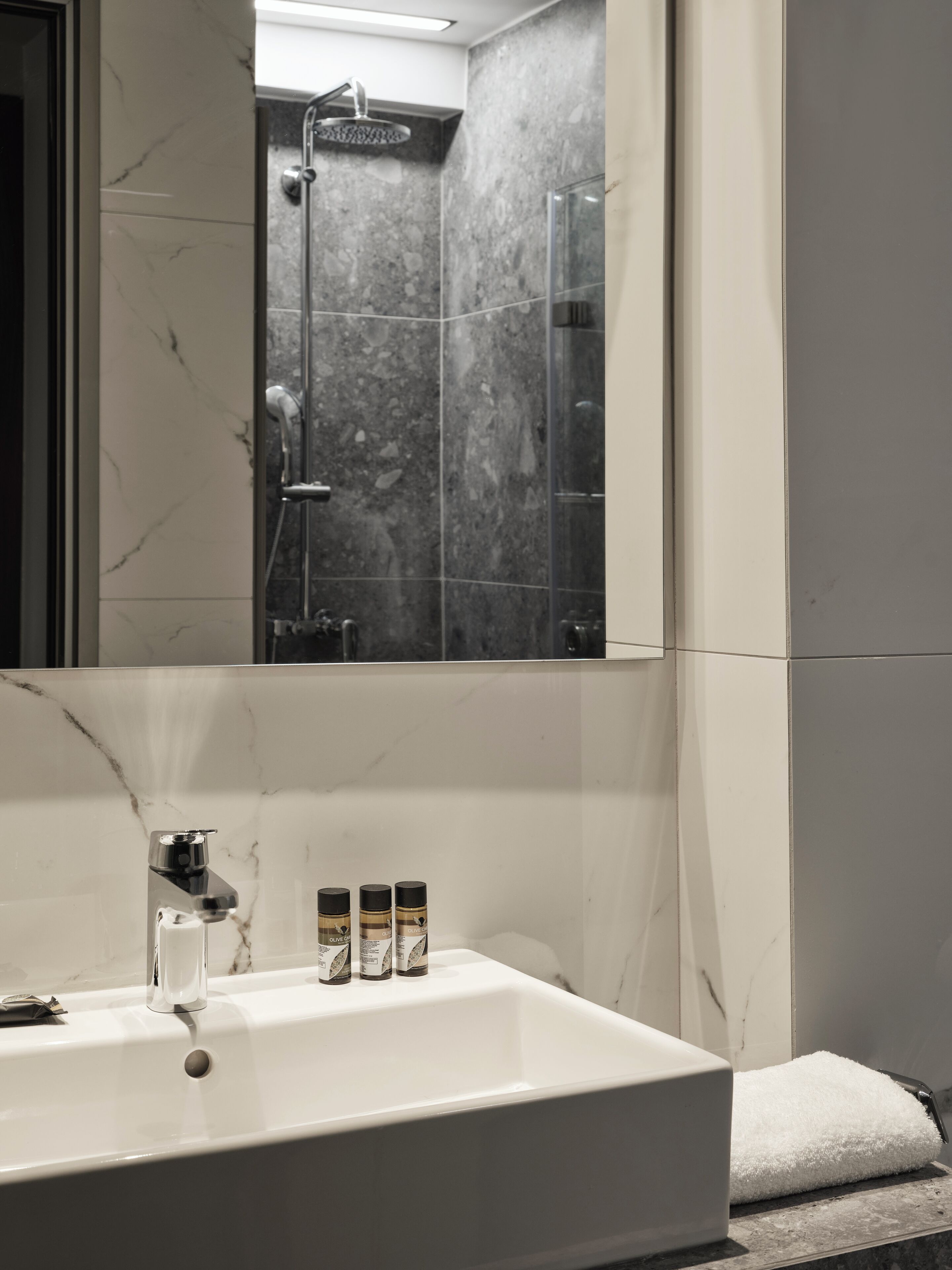 A bathroom with a large mirror, a white sink, and a shower area.
