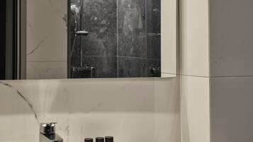 Une salle de bain avec un grand miroir, un lavabo blanc et un espace douche.