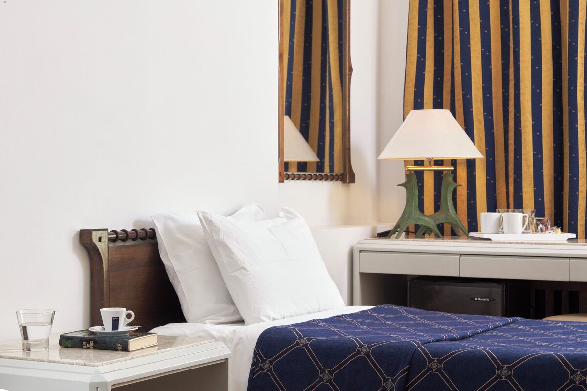 A hotel room with a bed, bedside table, lamp, and curtains.