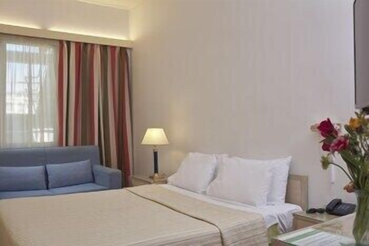 Habitación de hotel con cama, sofá, lámpara y un jarrón con flores.