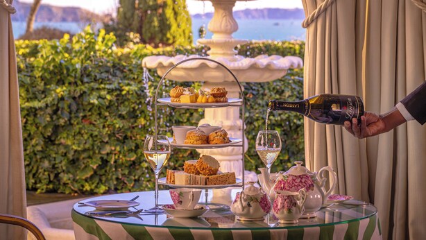 A table set with tea service, a tiered dessert stand, and a bottle of wine being poured.