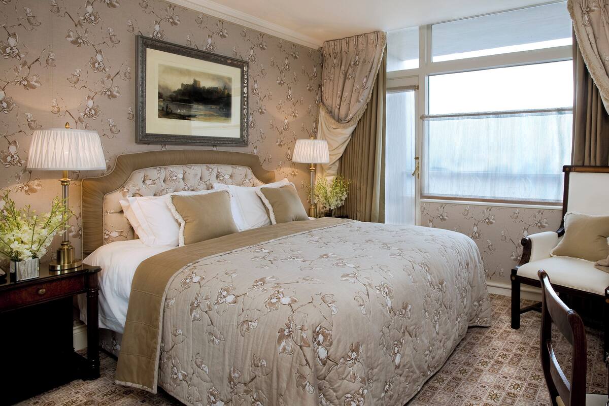 A bedroom with a large bed, two bedside tables, a chair, a window with curtains, and a framed picture on the wall.