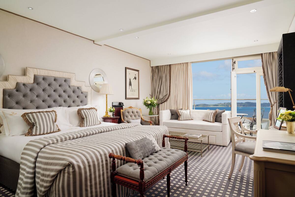 A hotel room with a large bed, a sofa, a desk, and a view of the sea.